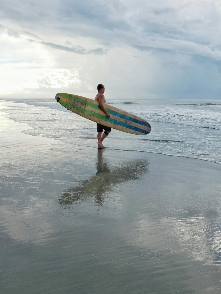 man walking into the ocean carrying a surfboard