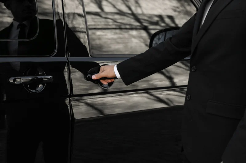 person in a suit opening a car door for another individual